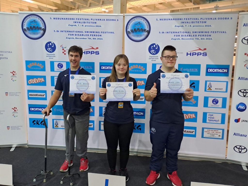 Festival plivanja za osobe s invaliditetom. Na slici su troje mladih ljudi. U sredini je djevojka, a sa njezine desne i lijeve strane su dječaci. U rukama drže diplome