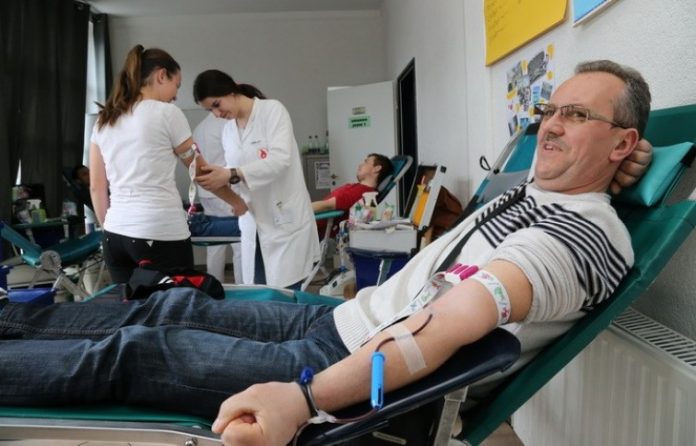 Muška osoba daruje krv, a u pozadini medicinska sestra uzima krv ženskoj osobi.