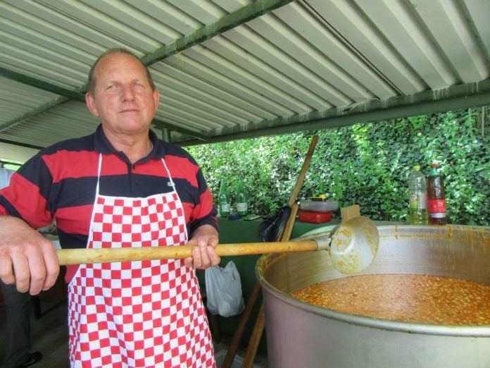 Kuhar Rudi Mesarić pred kotlom punog graha, u ruci drži šeflju