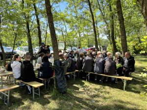Ljudi koji su došli kušati prvomajski grah sjede na klupicama i razgovaraju.