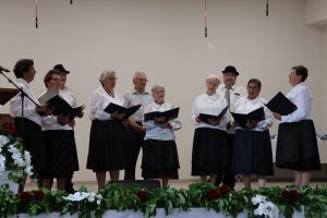 Muške i ženske osobe u nošnjama nastupaju i pjevaju na pozornici