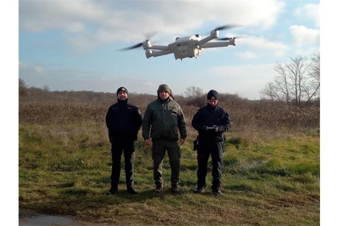 Policijski službenici PU međimurske stoje u šumi na zelenoj površini. Iznad njih nalazi se novi dron, koji ima svrhu za nadzor nezakonite sječe šuma